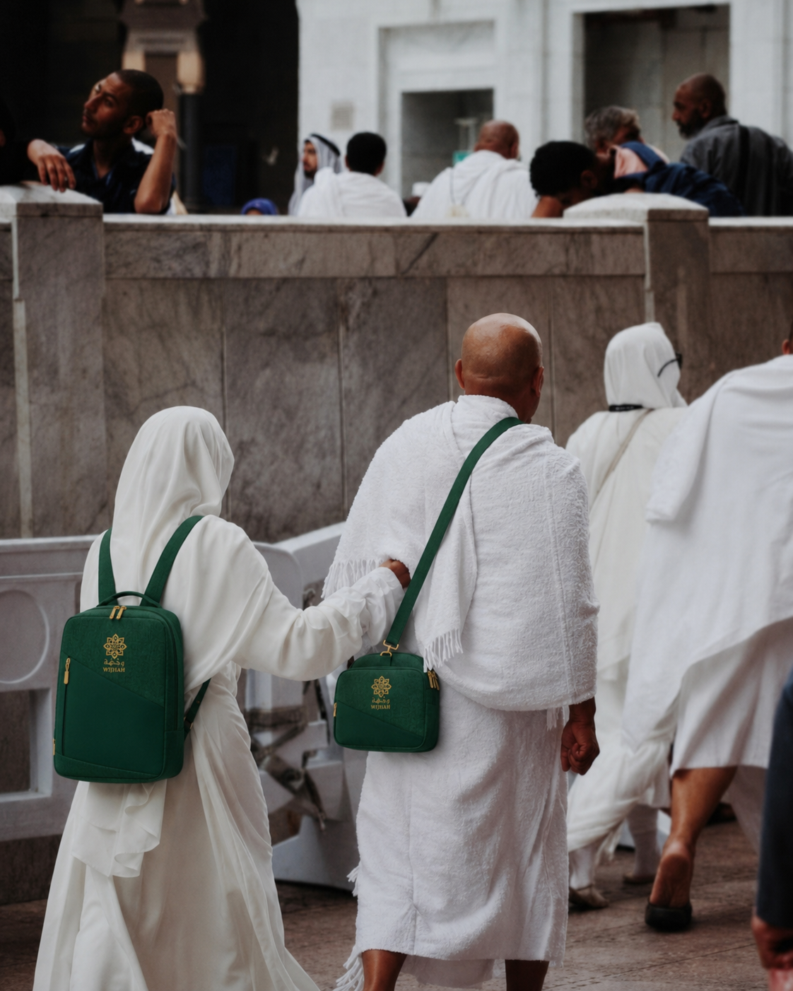 Two pilgrims in ihram at the Haram carrying green WIJHAH bags